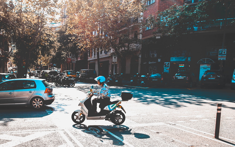 plant, sunlight, car, scooter, outdoors, wheel, apparel, built structure, city, road, vespa, clothing, ride, day, land vehicle, moped, building exterior