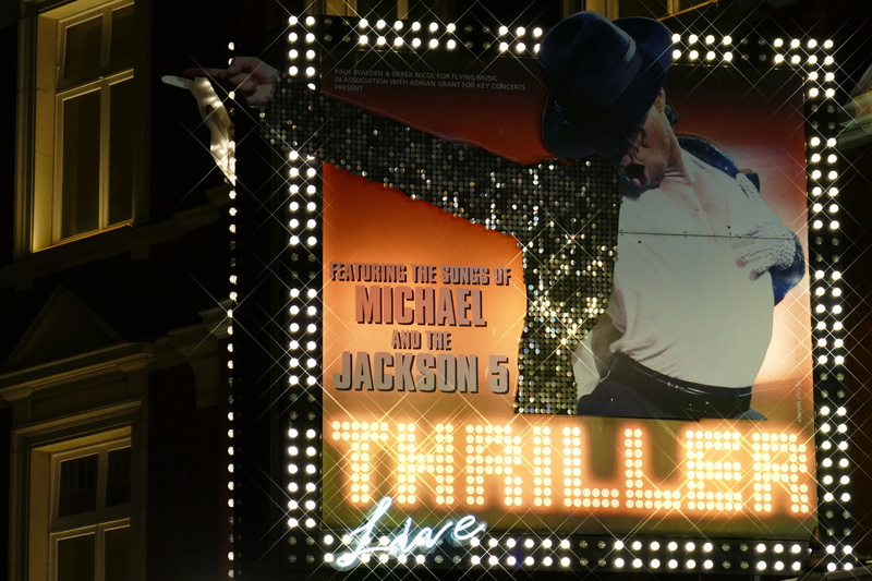 western script, real people, lighting equipment, nighttime, building, text, building exterior, billboard, outdoors, michael, skyscraper, sign, night, human representation