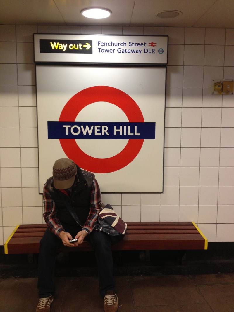 information, tile, sitting, subway station, train, england, person, western script, hat, one person, sign, obscured face, london, leisure activity, real people