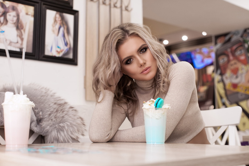 chair, short tops, sitting, brown eyes, cafeteria, looking at viewer, portrait, hands in hair, table, 2K, women indoors, blonde, women, fur coats
