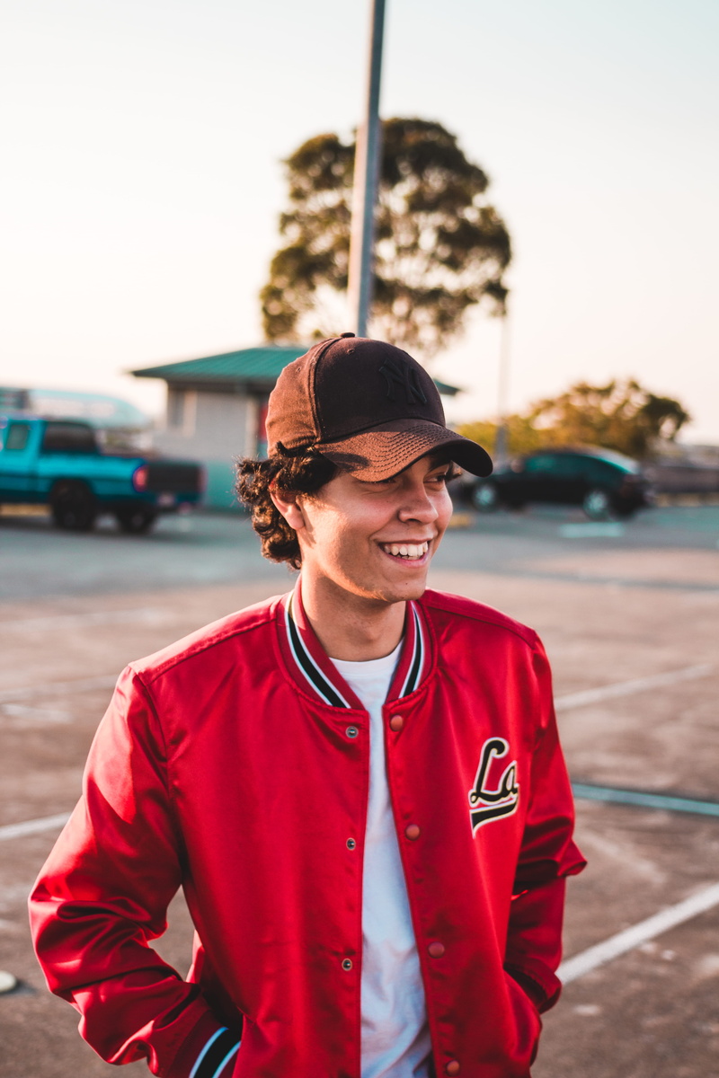 sunglasses, near, golden hour, one person, waist up, red, parking lot, fashion, car, clothing, person, smiling, front view, real people, lifestyles, human