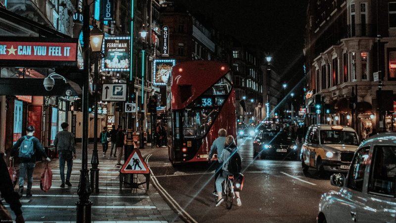 bicycle, io, bus, riding, land vehicle, pavement, transportation, street, buildings, cab, city, group of people, cars, man, road, car, light, red bus, time