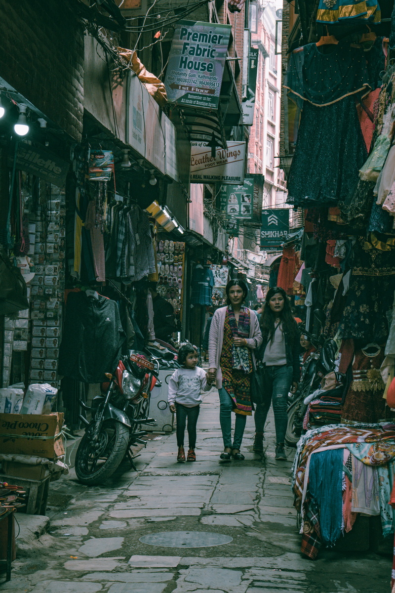 stalls, merchandise, mode of transportation, building exterior, retail, clothing, sale, street, motorcycle, pathway, wear, assorted, daylight, sell, shops