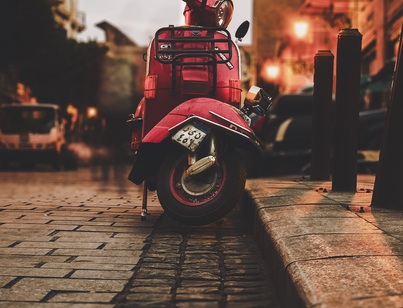 parking, apparel, toy, night, person, focus on foreground, incidental people, mode of transportation, motor scooter, sidewalk, automatic, vespa, paving stone