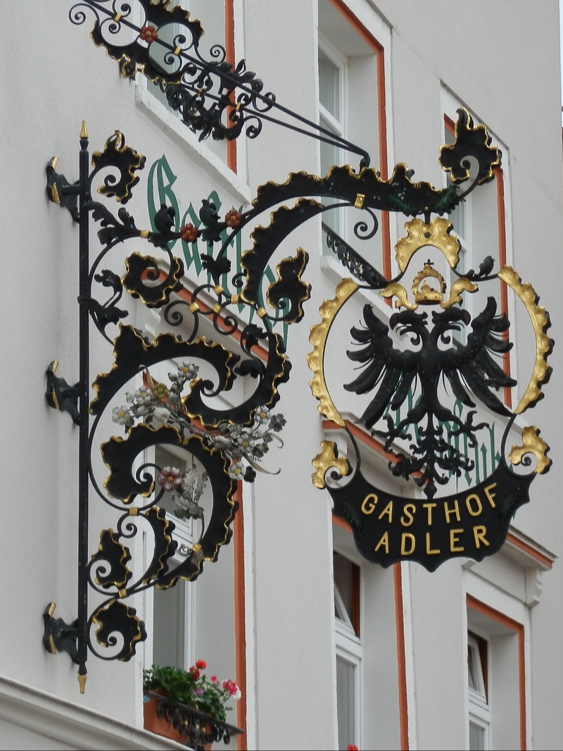 blacksmithing, building exterior, outdoors, western script, built structure, communication, wrought iron, staircase, door, day, golden, text, coat of arms