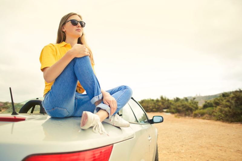 sunglasses, blue sky, hairstyle, one person, transportation, blonde, yellow polo shirt, adult, folded legs, beautiful woman, hair, street, glasses, voyage