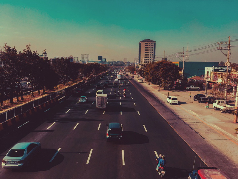 car, sky, trees, buildings, people, plant, building exterior, electric posts, built structure, automobiles, cityscape, street, high angle view, city street