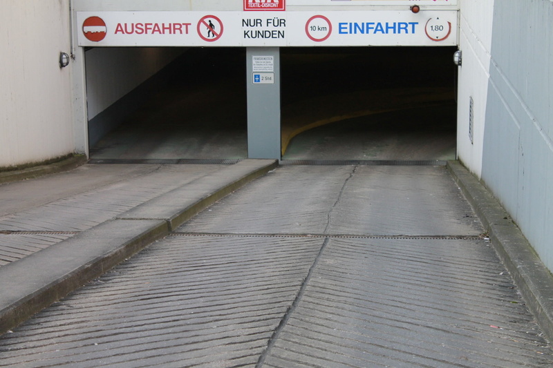 day, underground car park, communication, building exterior, text, no people, direction, footpath, downhill, symbol, city, western script, sign, outdoors