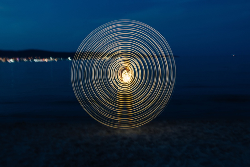 outdoors, painting, spiral, on the beach, 5K, shape, light, spinning, ocean, concentric, reflection, water, dusk, beach, pattern, nigh, sea, wire wool