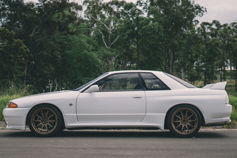 city, siding, coupe, stationary, plant, day, halter, parking, road, transportation, hubcap, motor vehicle, street, nature, car wheel, trees, wheel, grey