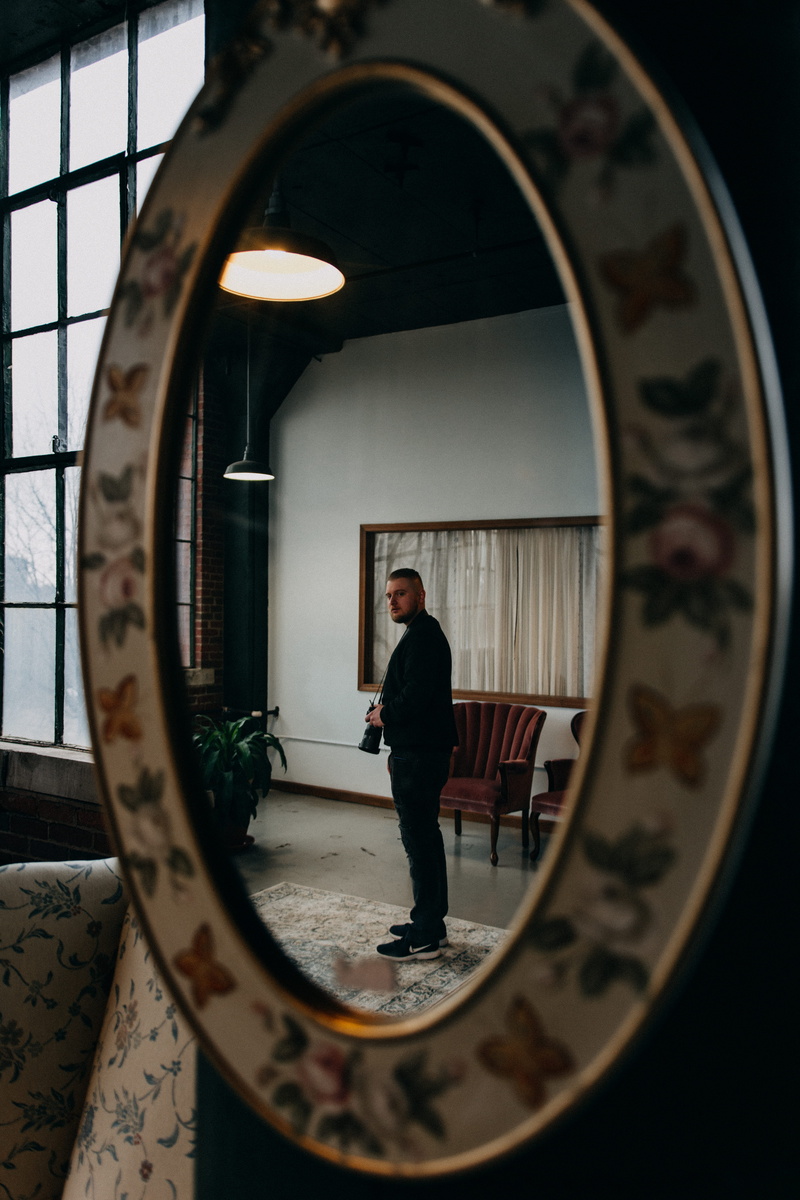 rubber shoes, plant, chairs, indoor plants, mirror, reflection, person, black jacket, sneakers, looking, building, furnitures, carpet, arch, wear, male