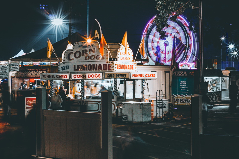 lighting equipment, time, outdoors, dogs, tree, food, beside, illuminated, lights, assorted, sign, neon, city, event, cocoa cola, corn dog, dark, arts culture and entertainment