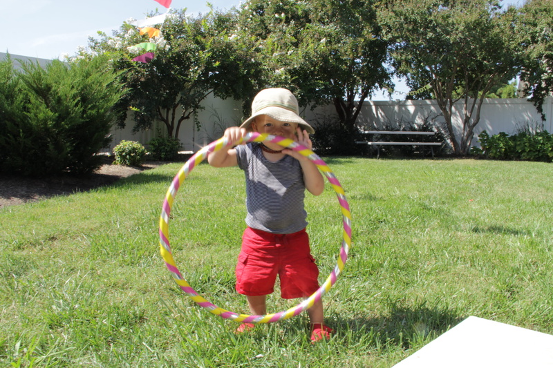 front or back yard, casual clothing, sunlight, fun, play, hula hoop, one person, child, kids, outdoors, tree, green color, standing, full length, spraying