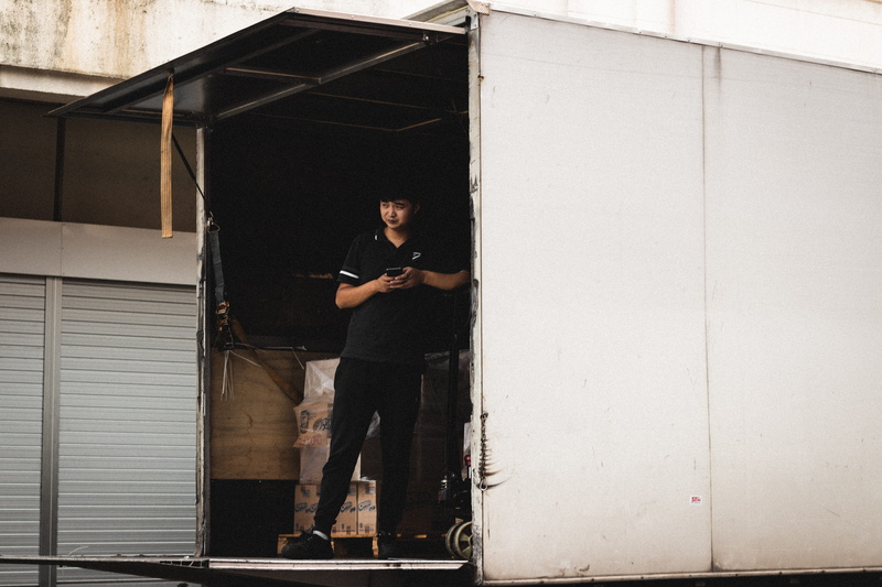 human, one person, built structure, shipping container, front view, holding, wireless technology, architecture, man, transportation, overcoat, smart phone