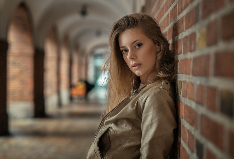 brown hair, standing, contemplation, one person, waist up, 1080P, jacket, women, leather jackets, depth of field, hairstyle, young adult, brick, portrait