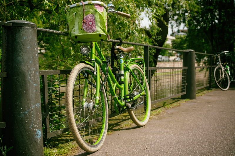 sidewalk, parked, water, gree, growth, railing, stationary, bike, basket, park, pavement, parking, protection, outdoor, no people, leaning, riding, metal
