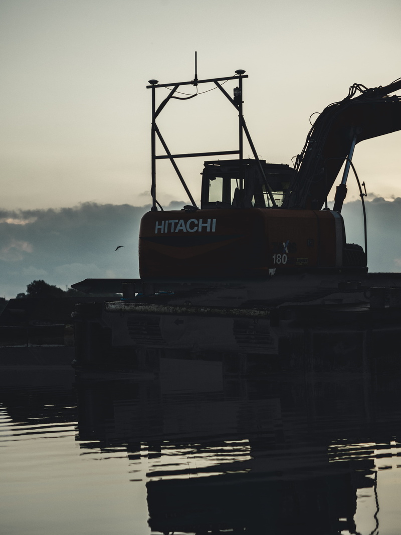 sky, barge, mode of transportation, bulldozer, architecture, waterfront, watercraft, transportation, vessel, yacht, built structure, clothing, outdoors