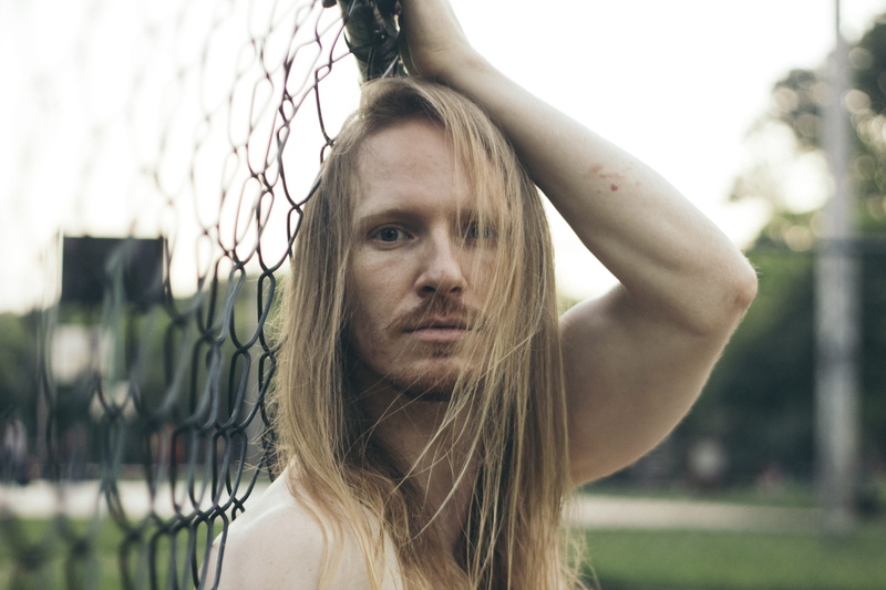 cyclone fence, outdoor, boundary, portrait, pose, long hair, adult, person, close-up, daytime, daylight, real people, holding, lips, blond hair, headshot