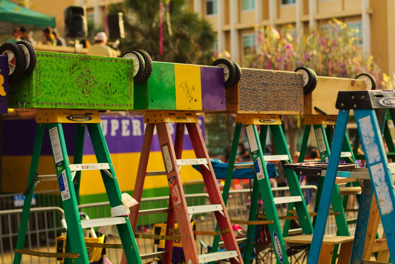 mode of transportation, selective focus, green color, no people, carnival, large group of objects, text, gras, mardi, in a row, focus on foreground, architecture