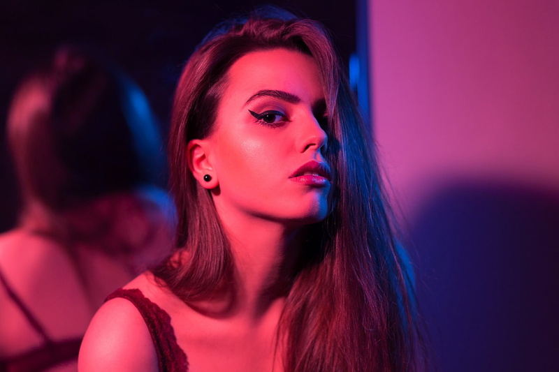 brunette, hair in face, looking at camera, hair, hairstyle, looking at viewer, headshot, purple, pink, one person, portrait, mirror, nightlife, nightclub