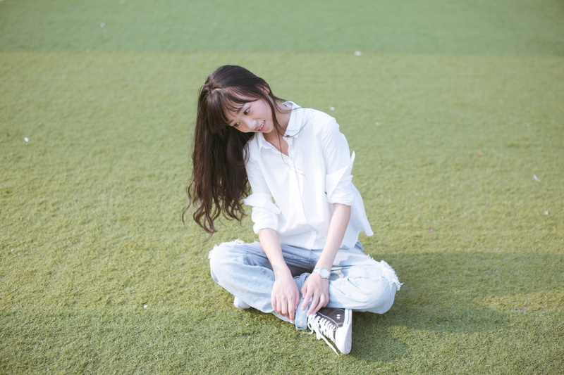 adult, young adult, grass, hairstyle, real people, one person, green color, land, day, happy, hair, person, lifestyles, sitting, leisure activity, long hair