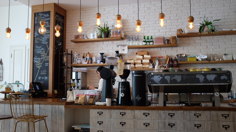 large group of objects, indoors, woman, day, business, coffee shop, coffee, 2K, behind, arrangement, counter, bar - drink establishment, container, job