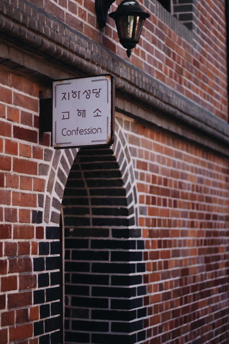 western script, concrete, door, confessing, built structure, building exterior, brick, wall, no people, catholic, white, information, seoul, architecture