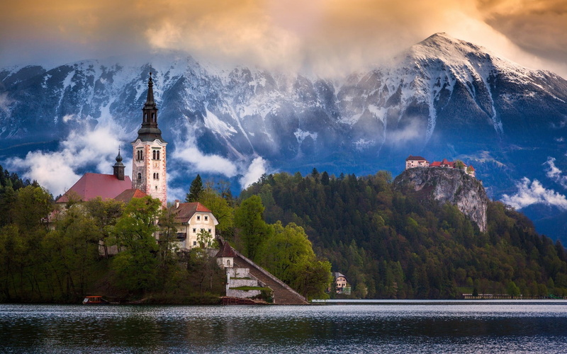 cloud - sky, travel destinations, tower, water, mountain, near, beauty in nature, religion, built structure, outdoors, mountain range, building, scenics - nature