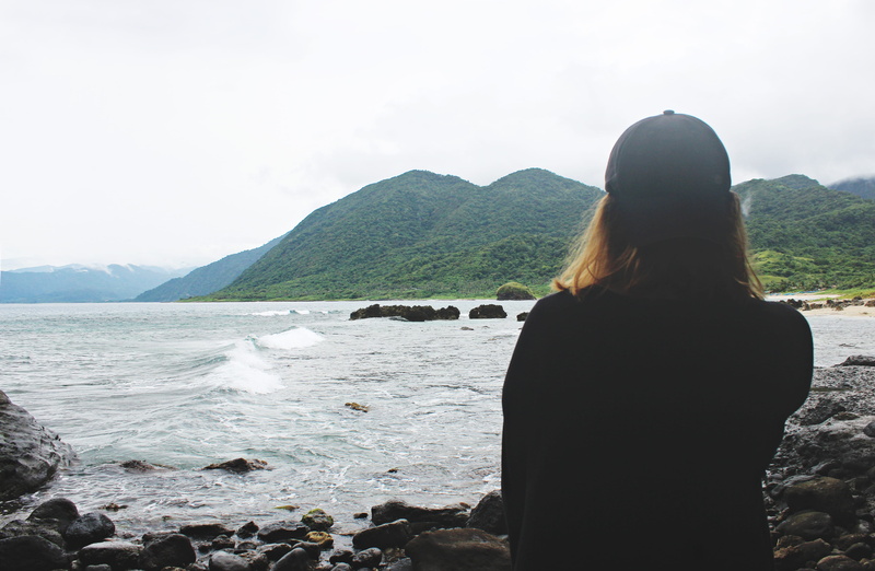 waist up, standing, one person, leisure activity, sea, nature, hairstyle, real people, looking at view, solid, outdoors, mountain, rear view, rock, water