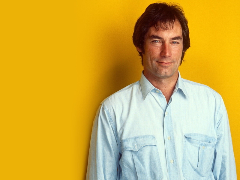 studio shot, portrait, adult, casual clothing, indoors, yellow background, one person, men, waist up, brown hair, Timothy dalton, Eyes, smiling, Smile