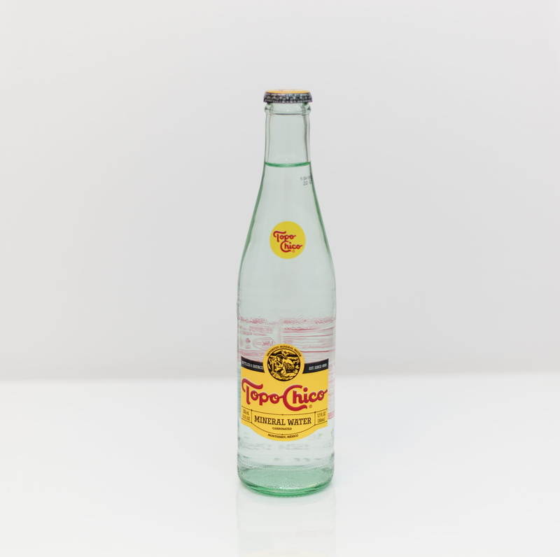 drink, indoors, food and drink, text, communication, bottle, spoke, liquor, white background, topo chico, no people, transparent, container, cocktail, western script
