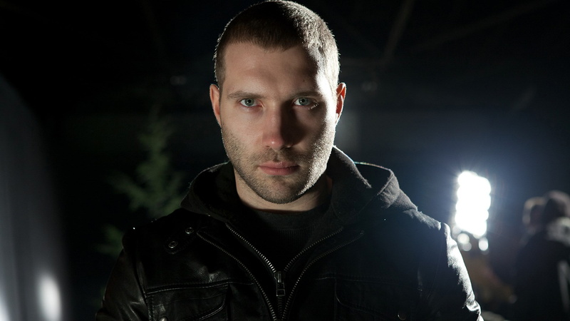 headshot, dark, looking at camera, front view, serious, portrait, beard, focus on foreground, aggression, night, jacket, young adult, standing, adult, confidence