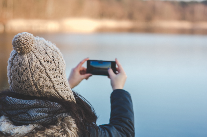 wireless technology, water, communication, holding, one person, smart phone, hat, phone, photographing, activity, warm clothing, rear view, mobile phone