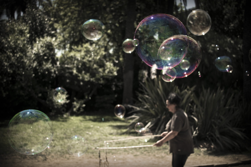 standing, side view, offspring, people, adult, interaction, males, soap sud, exploration, planet, holding, daytime, outdoors, bubble wand, mid-air, one woman only