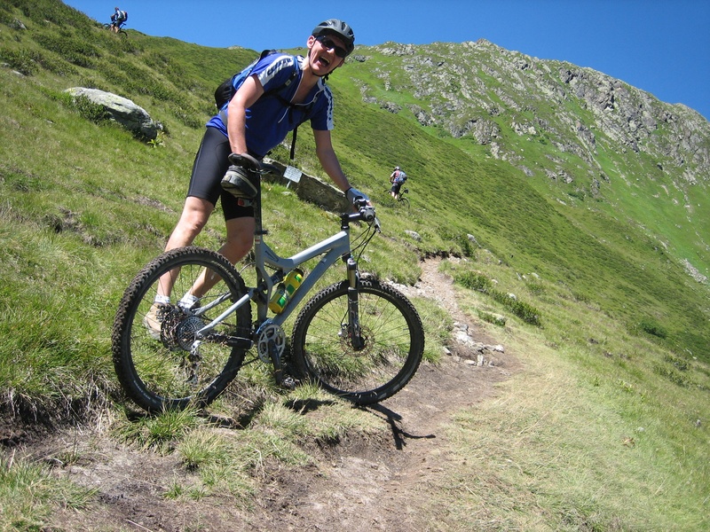 helmet, land vehicle, holding, headwear, ride, mtb, outdoors, grass, adventure, leisure activity, green color, beauty in nature, mountains, sport, mountain bike