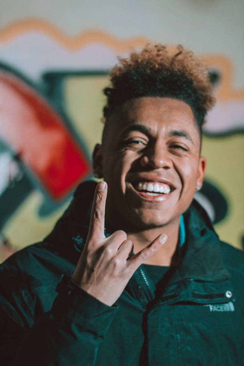 horn, person, lifestyles, gesturing, looking at camera, 5K, real people, rock, roll, indoors, happiness, teeth, jacket, focus on foreground, man, hairstyle