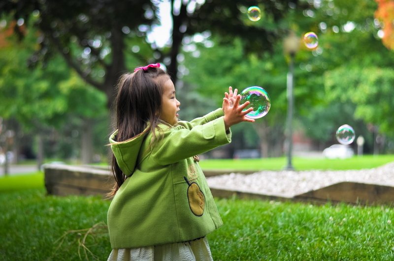 blowing, grass, kid, smiling, bubble wand, hair, female, focus on foreground, bubbles, playful, green color, playing, green, 2K, happiness, nature, asian