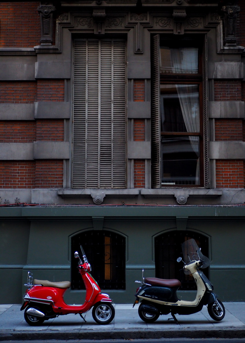 brick, stationary, window, motor, facade, building exterior, land vehicle, outdoors, day, two, motorcycle, near, no people, vespa, red, city, mode of transportation