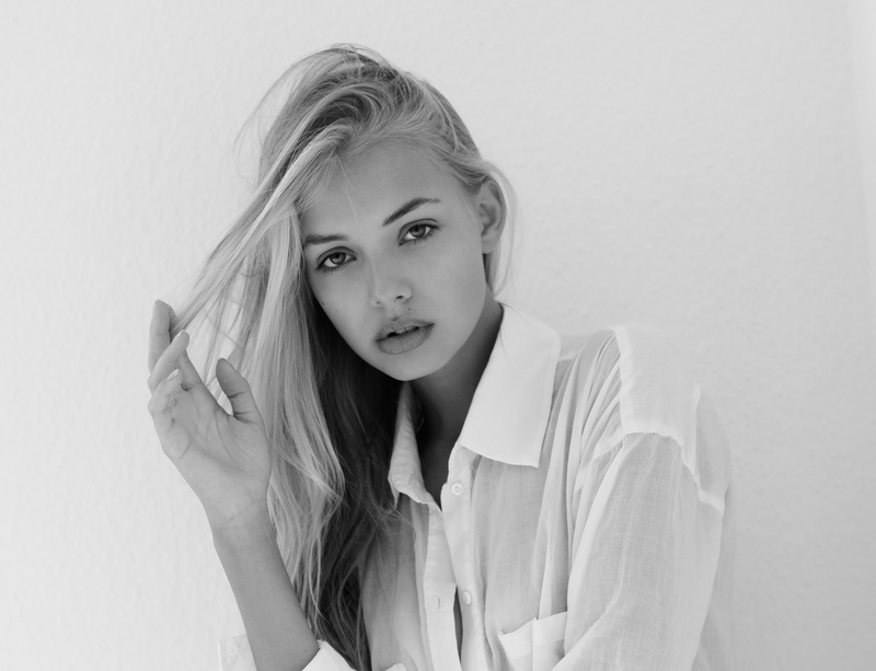 long hair, monochrome, contemplation, blond hair, teenager, beautiful woman, holding hair, indoors, touching hair, front view, face, young adult, hairstyle