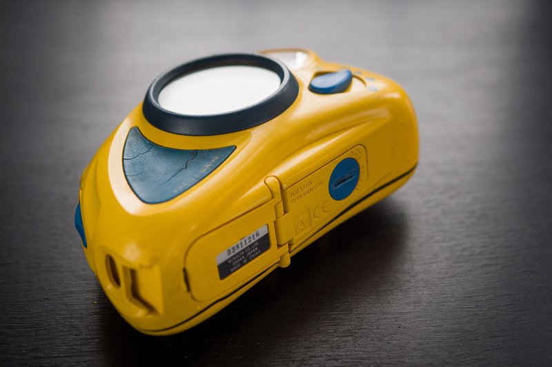 toy car, strap, technology, cd player, indoors, studio shot, tape, motor vehicle, accessories, vehicle, toy, yellow, goggles, camera, close-up, digital camera