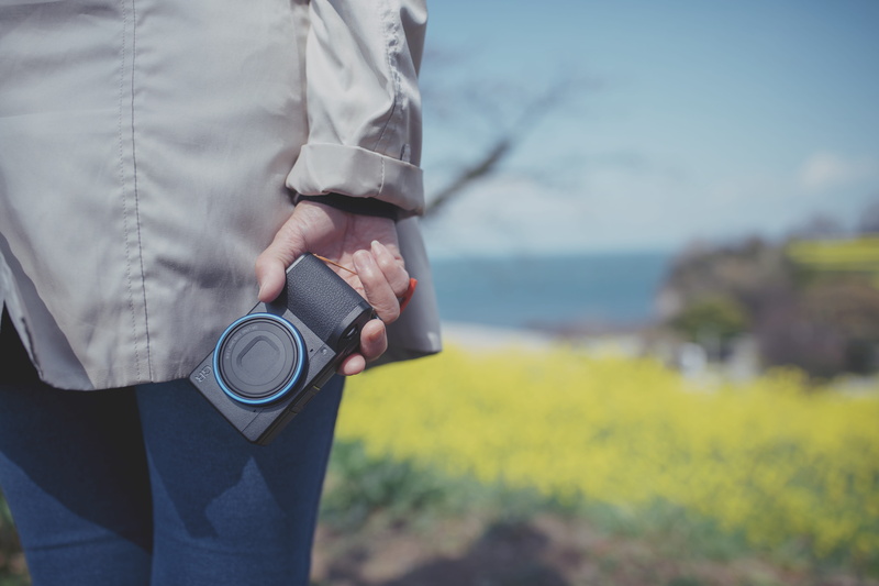 person, focus on foreground, sleeve, camera lens, ipod shuffle, mobile phone, clothing, camera, shoot, human hand, holding, human, men, water, casual clothing
