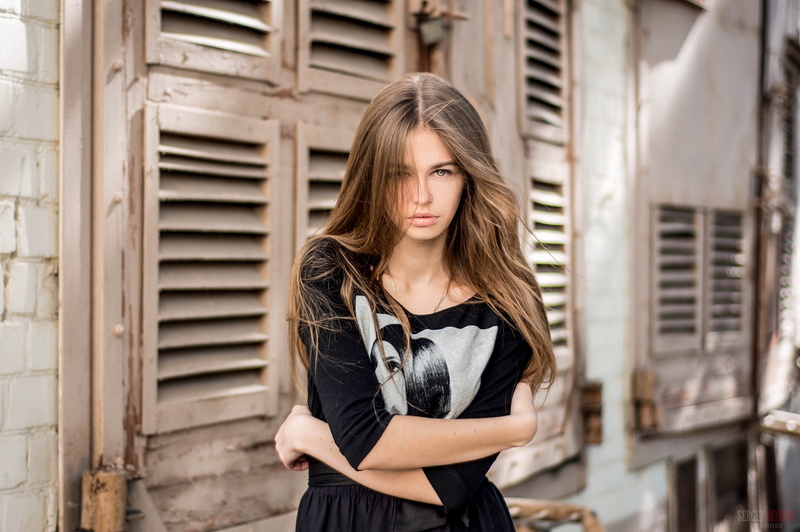 hair in face, depth of field, women, front view, standing, emotion, arms crossed, adult, long hair, juicy lips, waist up, beauty, 1080P, one person, architecture