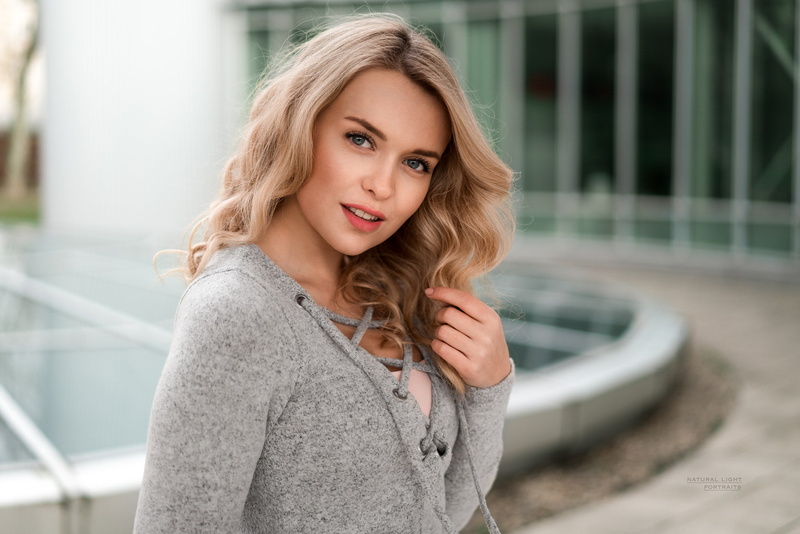 outdoors, one person, real people, looking at camera, hair, looking at viewer, beauty, blonde, portrait, face, grey clothing, touching hair, front view