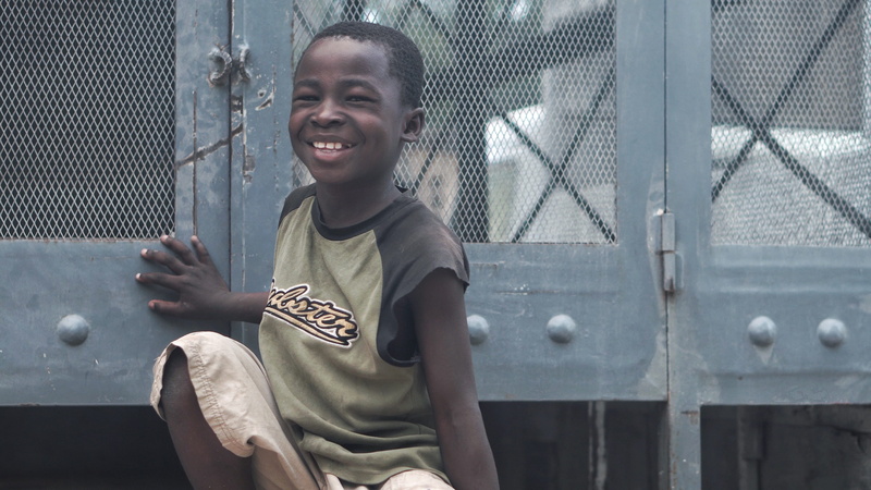 travel, boy, kid, men, child, front view, haiti, day, smile, smiling, outdoors, pants, truck, beside, casual clothing, hatian, pose, childhood, gray, black