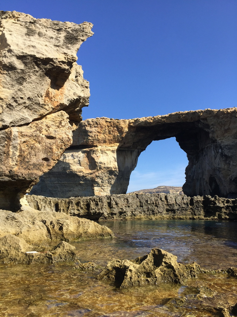 beauty in nature, clear sky, sunlight, eroded, gozo, sky, day, rock formation, water, rock - object, solid, tranquil scene, rock, physical geography, tranquility