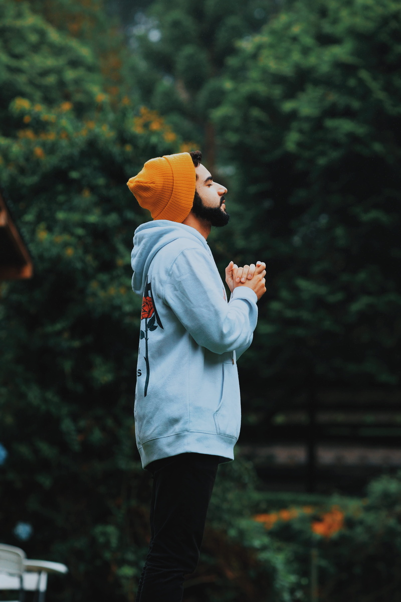 knit cap, casual clothing, posing, wearing, lifestyles, side view, outdoors, tree, standing, blur, wear, focus on foreground, pray, one person, real people
