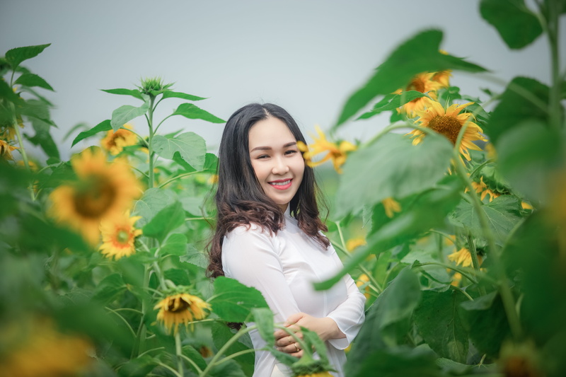 ao dai, sunflowers, wearing, photoshoot, one person, smile, beautiful, hairstyle, park, field, nature, fashion, long hair, traditional wear, standing, 5K