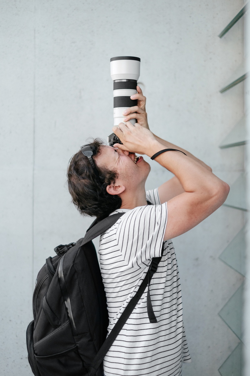 telephoto lens, one Person, dslr, white, wall - building feature, holding, using, young Adult, outdoors, wireless technology, people, lifestyles, man, backpack