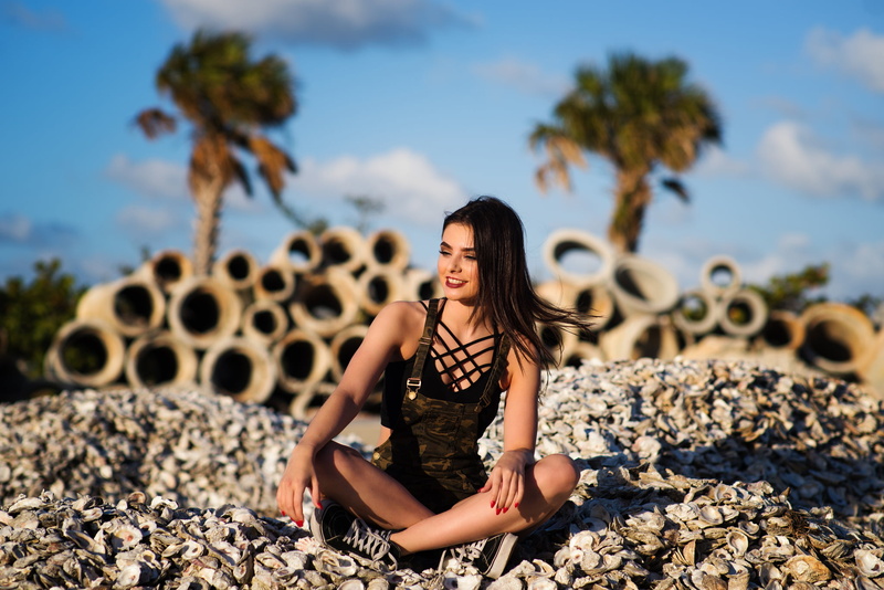 rock, sitting, day, sky, sunlight, hair, depth of field, overalls, sneakers, women outdoors, casual clothing, one person, full length, solid, looking away
