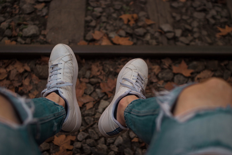 sitting, rail, leisure activity, feet, railway, railroad track, pebble, real people, jeans, one person, land, body part, personal perspective, fitted, leg